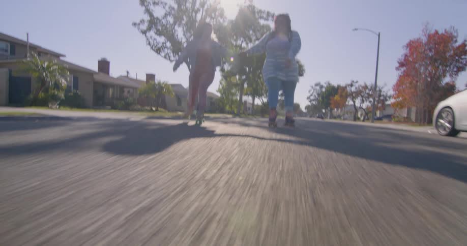 Two friends hold hands while roller skating on the neighborhood streets at morning