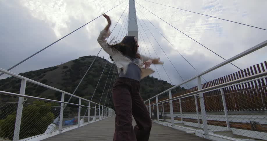 A young woman is dancing on a bridge in the day time
