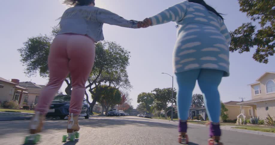 Two friends hold hands while roller skating on the neighborhood streets at morning