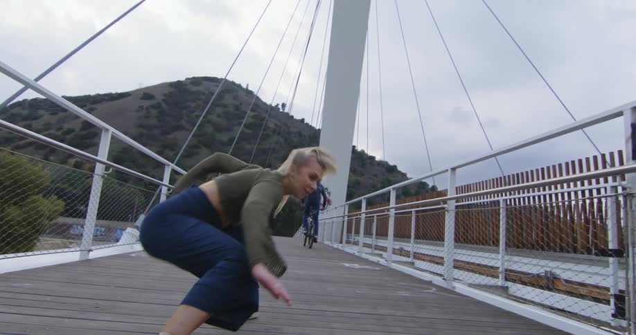 A young woman is break dancing on a bridge in the middle of the day