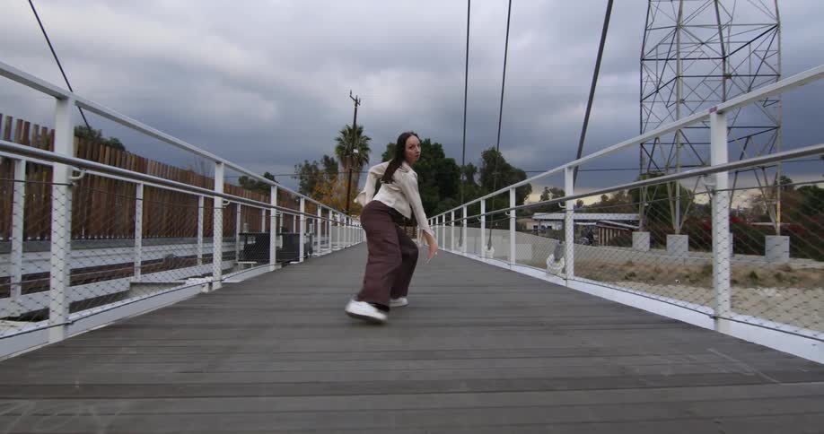 Young performer dances fluidly walking backwards over a suspension bridge