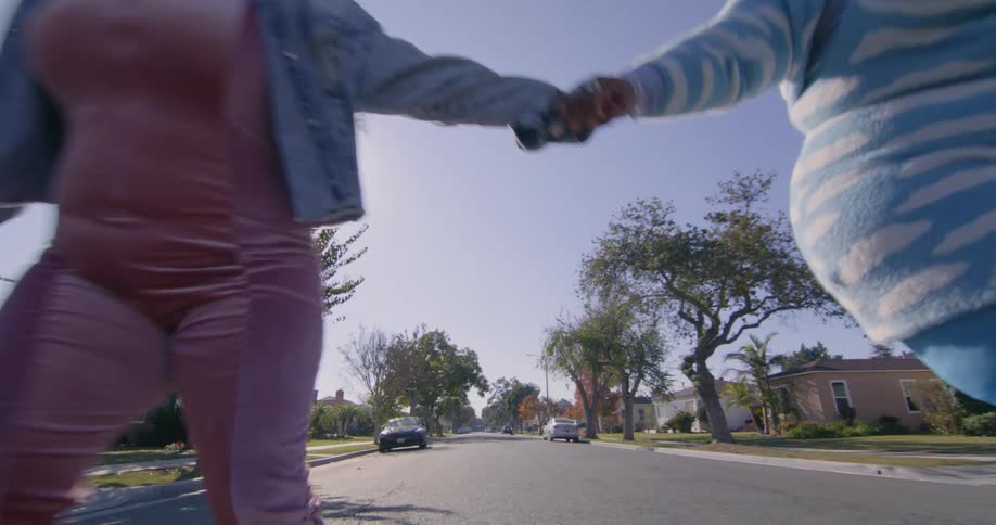 A pair of large women hold hands while roller skating down a road through a residential neighborhood on a sunny day