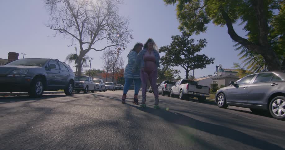 Two women roller skate down the street