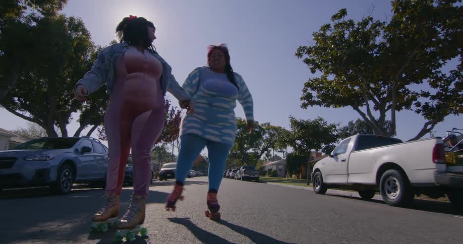Two women are holding hands while roller skating on a neighborhood street