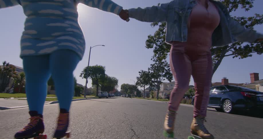 Two friends holding hands roller skating on the neighborhood streets