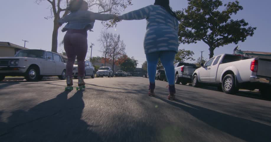 Friends are rollerblading outside in the street by some cars