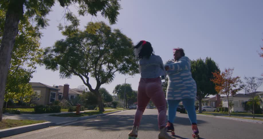 Two friends spinning on roller skates in a neighborhood street