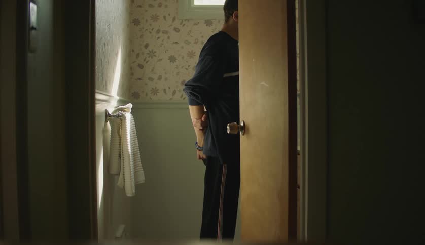 A teenage boy stands in a room and shakes his leg as he looks around