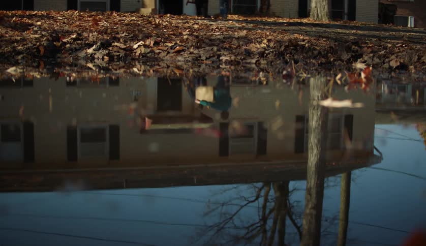 Puddle reflects two people carrying items into house
