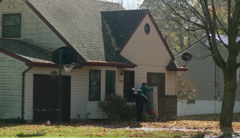 Man makes a shot through basketball hoop before moving to help older woman with mattress on house steps