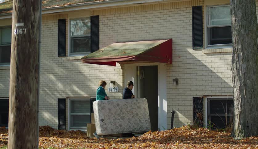 A teenage boy and his mother are carrying a mattress into an apartment building