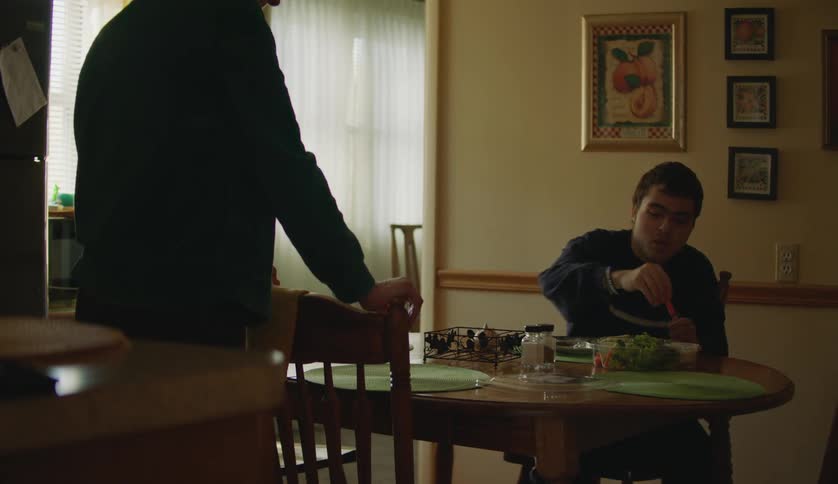 A young man is eating inside and talking to a family member