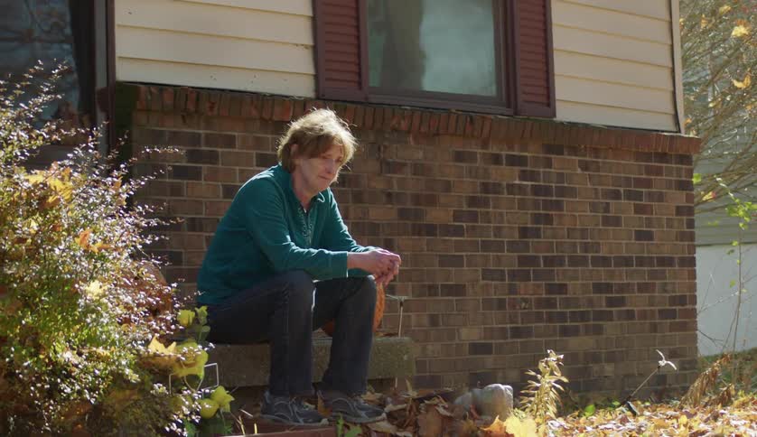A woman is sitting on her porch outside of her house
