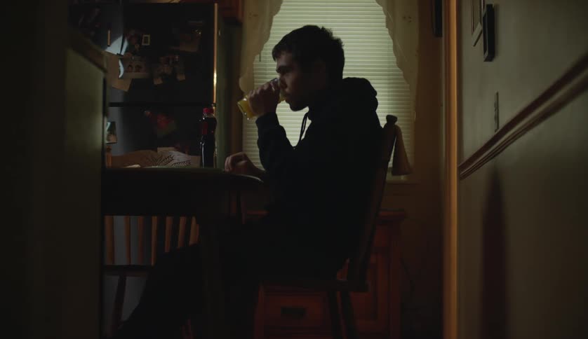 A young man is sitting down and drinking some orange juice