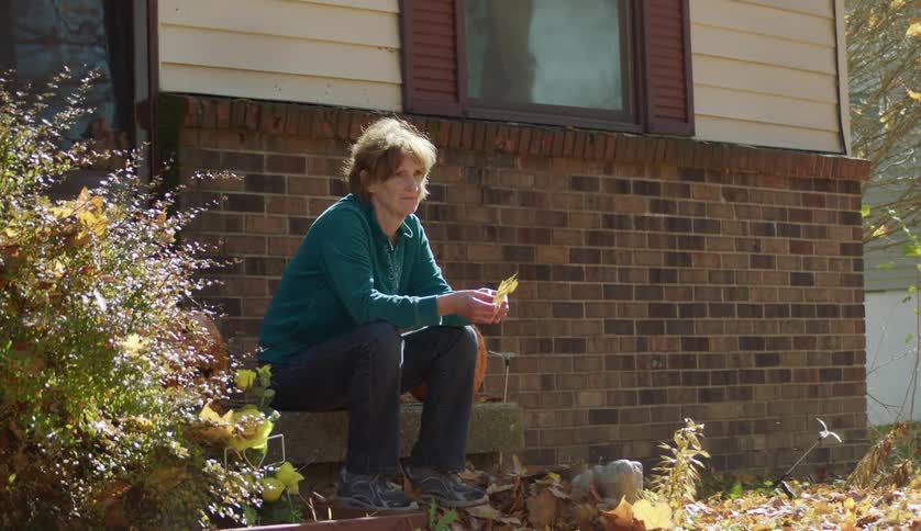 Mature woman sitting on the porch of the house playing with a dry leaf