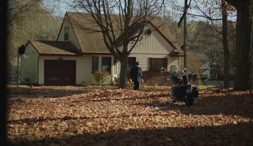 A teenage boy walks through the leaves covering his front yard as he goes to his house