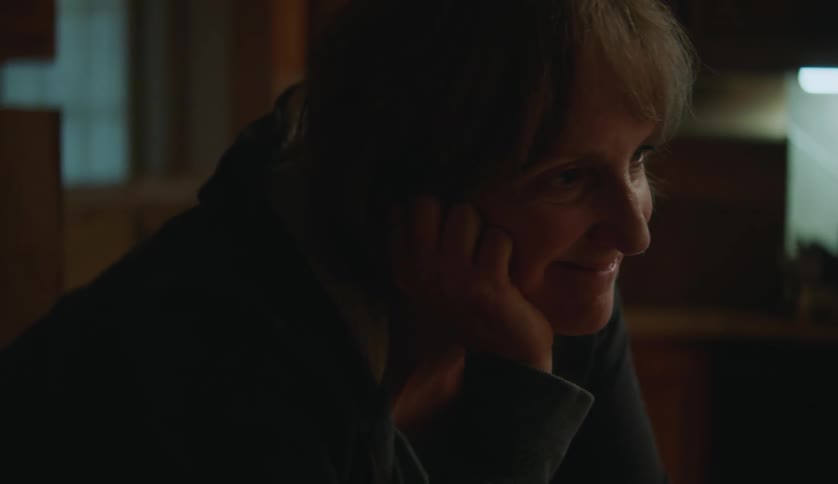 An older white woman is sitting down inside of her house