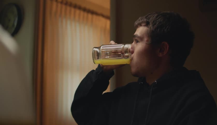 A mother walks in to a room as her teenage son quickly drinks a glass of orange juice