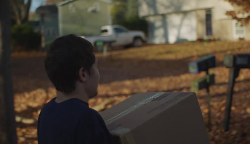 People carry cardboard boxes across street from one house toward another during fall