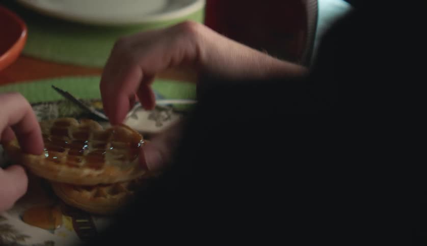 Man pours syrup on waffles before picking one up and tearing it in half with his hands