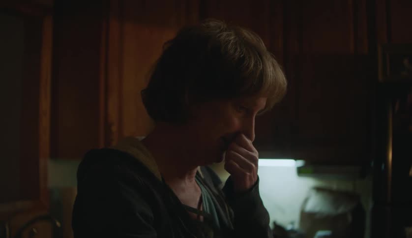 Tired mature woman rubs her eyes and face while talking in the kitchen at home