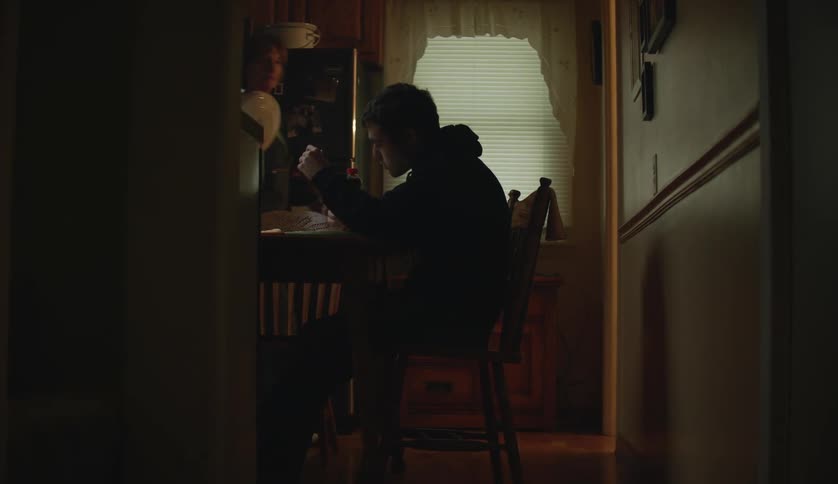 Womanwalks back and forth as young man sits at table eating