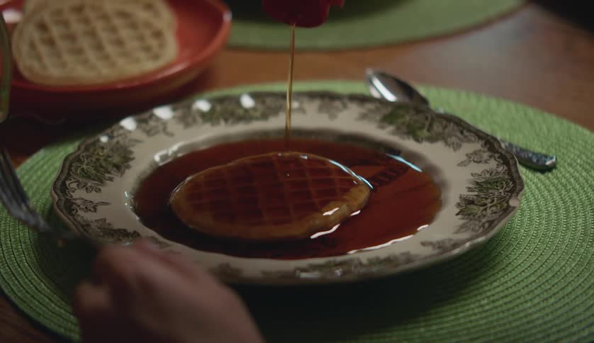 A person pours syrup all over their waffle
