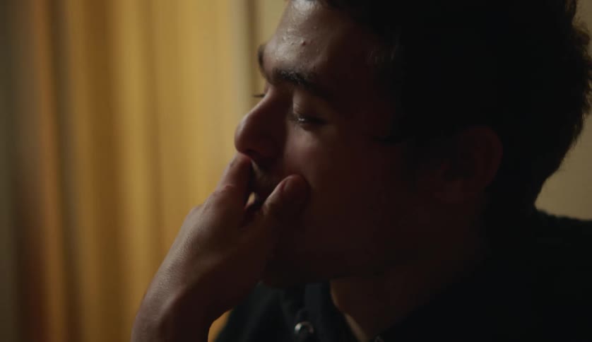 Close up of a man sitting on a room rubbing his mouth and head with his hand