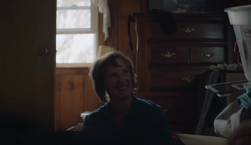 Older woman smiles as she sits in room throwing and catching ball with man
