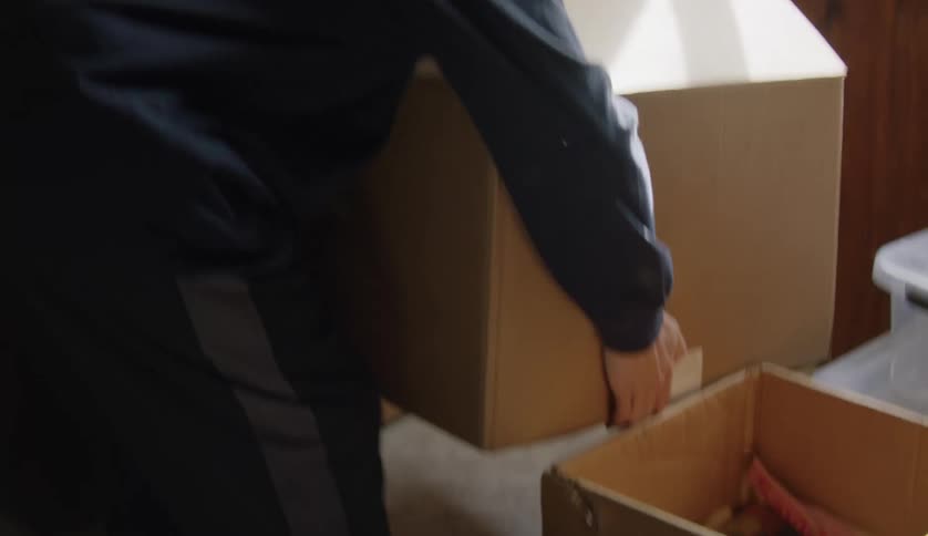 Man with dark blue hoodie carries boxes in room