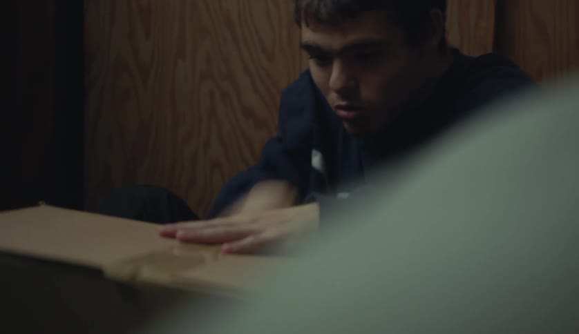 A young white man is taping up a box inside of his home
