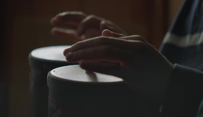 A person is sitting indoors and playing drums