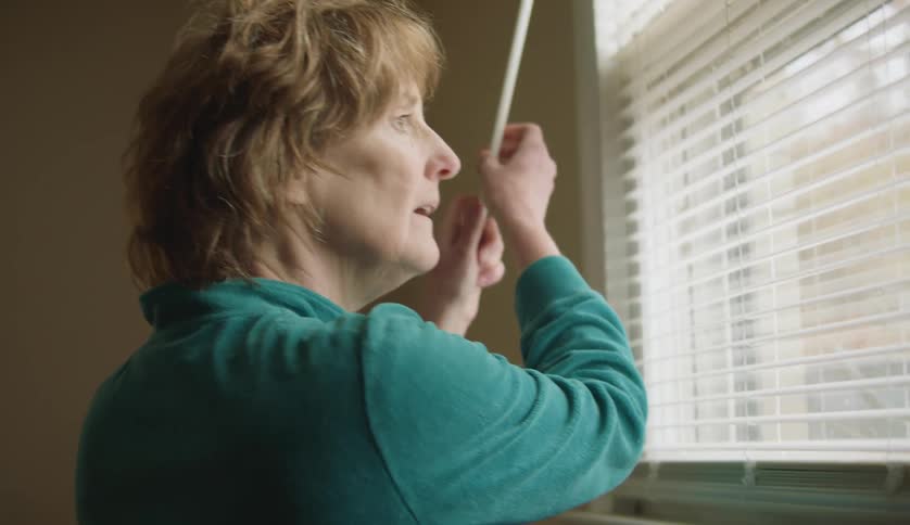 Mature woman turns the stick to open the window shades at home