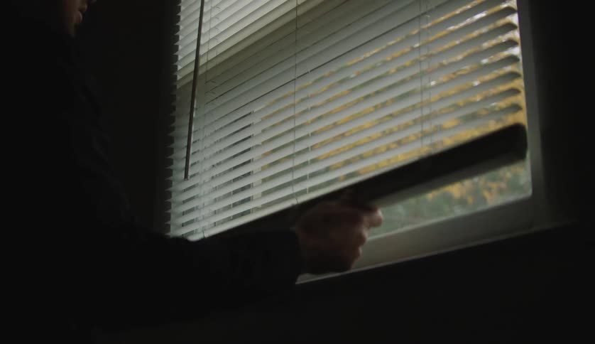 Silhouette of a person closing down the blinds on a window at home