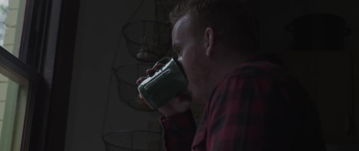 A man drinks from his mug while looking out a window