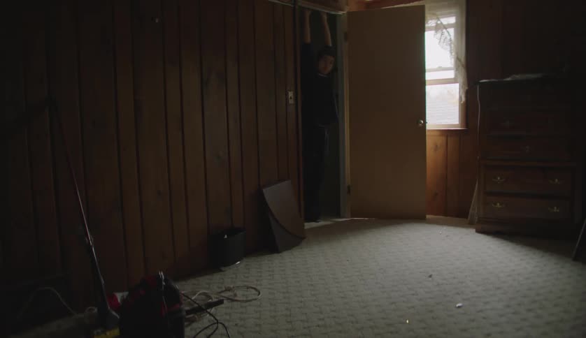 A teenage boy stands in the doorway of a room and holds on to the top and pulls himself up