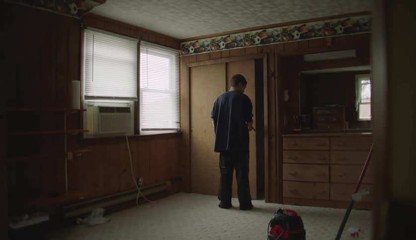 A young man enters and crosses a room to look into the closet