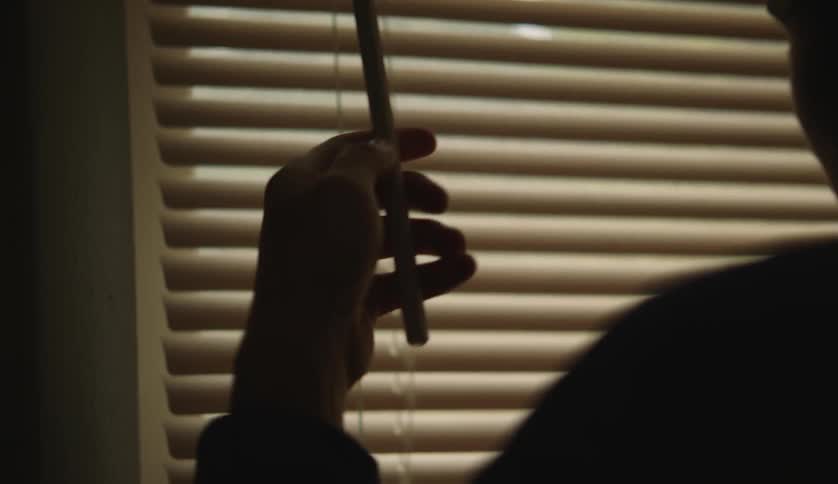 A person is closing their window blind
