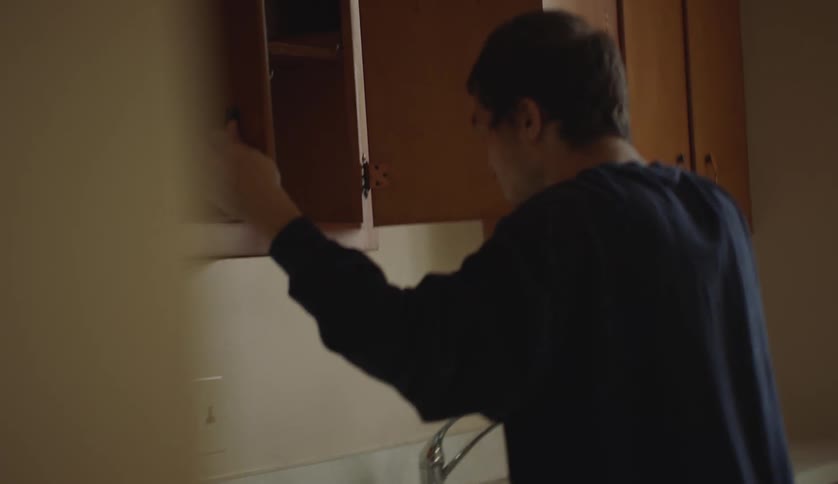 A young man is going through the cabinets inside of his kitchen