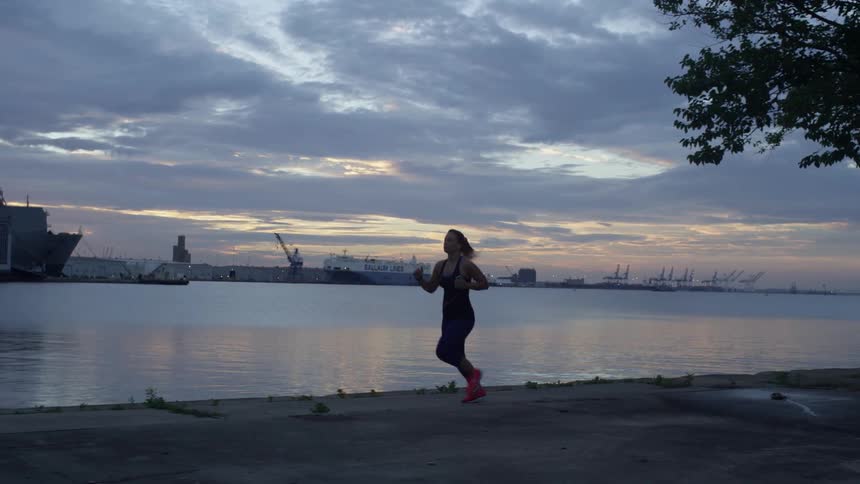 A woman is jogging along the shore at sunset