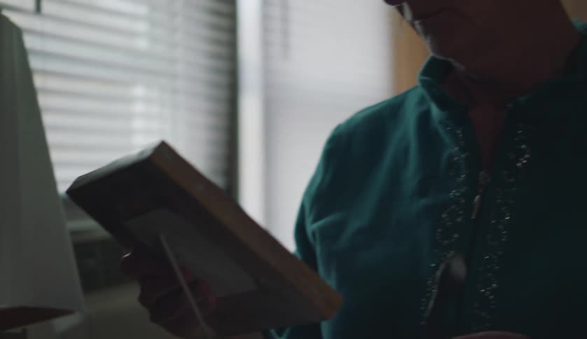A woman is cleaning up a room and she stops to look at a photograph in a frame on a shelf