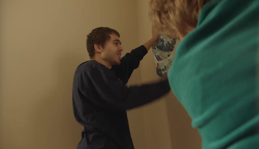 A teenage boy hangs a poster on the wall with help from his mother