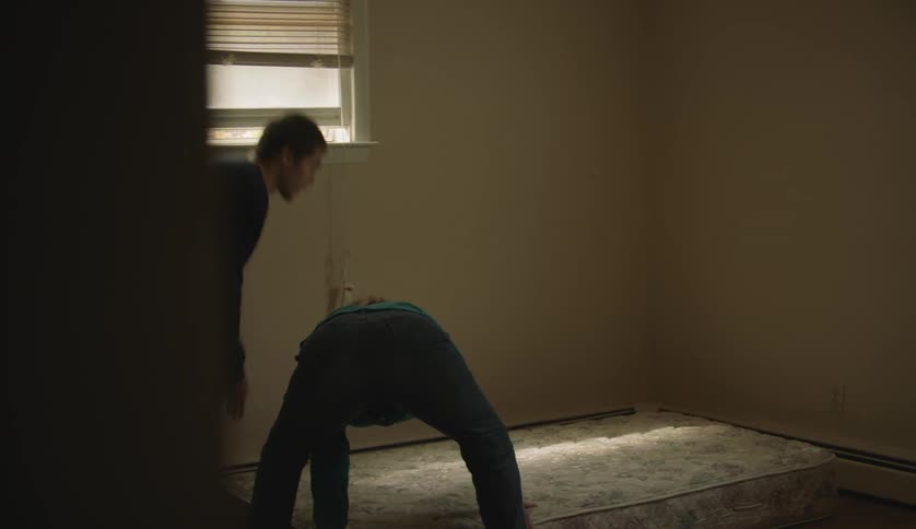 A teenage boy and his mother are moving a mattress into an empty room