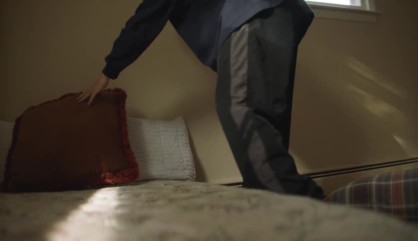 A young man places pillows on a bed indoors during the day