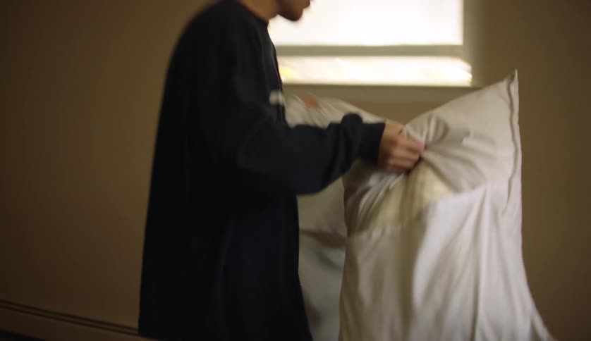 Young man with special needs puts pillows over a bed in the bedroom