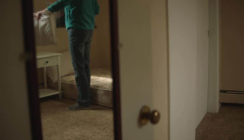 A woman carries a bunch of pillows into a small bedroom and pauses for a moment before placing the pillows on the bed
