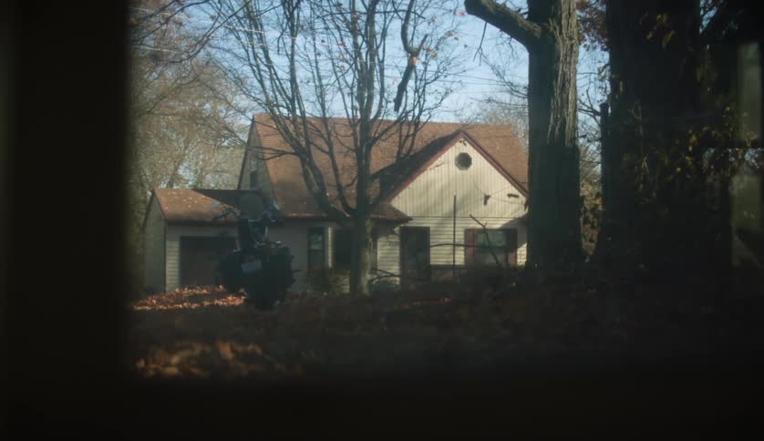 Window pane shows house yard and driveway full of fallen leaves