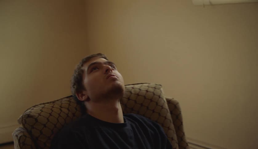 A young man stares at the ceiling while swiveling back and forth in a chair indoors during the day