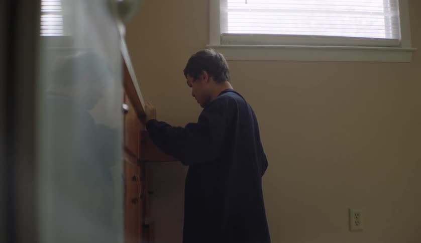 A young man kneels while searching through drawers in a home kitchen during the day