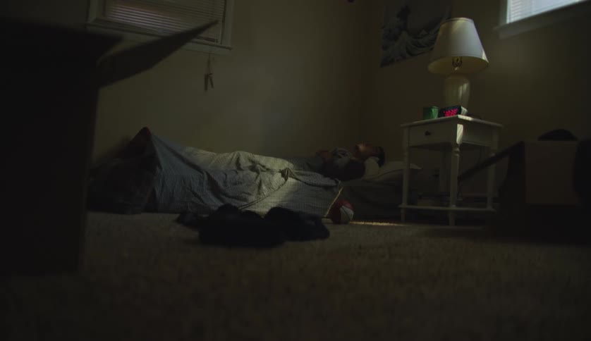 Man lies on mattress in dim carpeted room